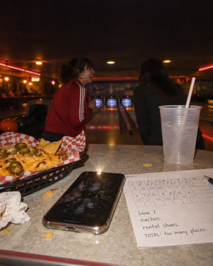 Smudged phone and a bowling scorecard reading lane 7, nachos, rental shoes, total too many places